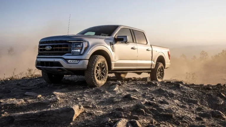 The Ford F-150 Tremor sits parked on a rocky surface. The truck is light grey. We see it from a front quarter angle, facing to our left.