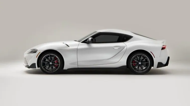 The 2023 Toyota GR Supra sits parked against a white background. The car is white. We see it in profile, facing to our left.