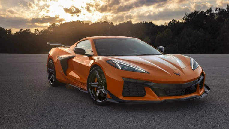 A 2023 Corvette Z06 Coupe is parked on a tarmac. It is orange. We see it from a front quarter angle, facing slightly to our right.